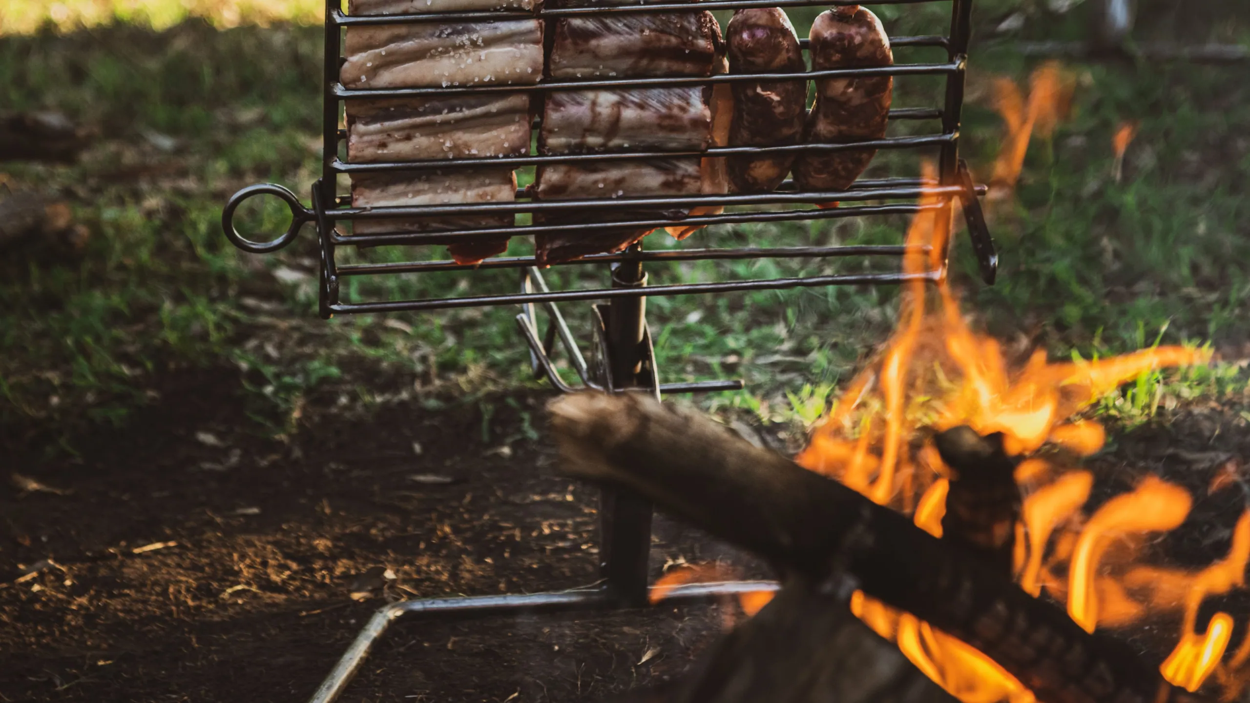 Ribs and chorizos on a Sostiene asador beside a live flame at dusk