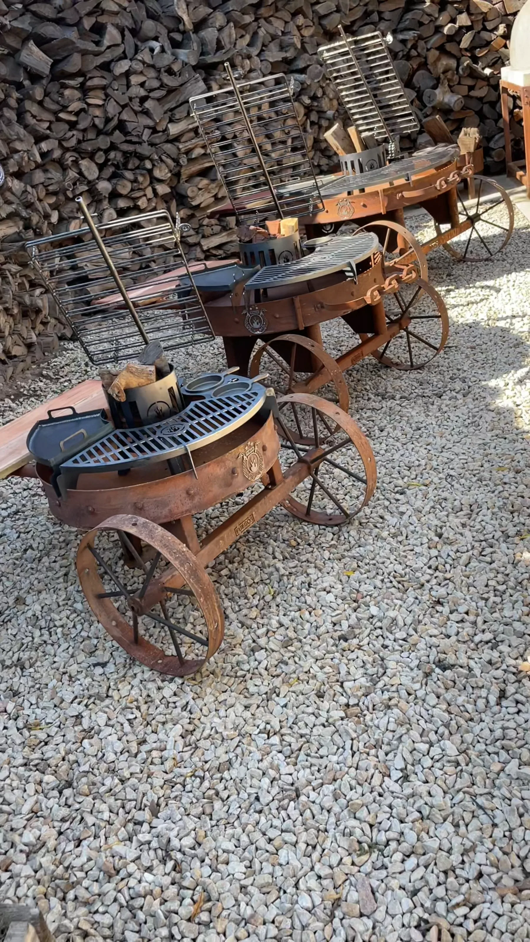 Three Alamo grills lined up against the woodpile at the workshop