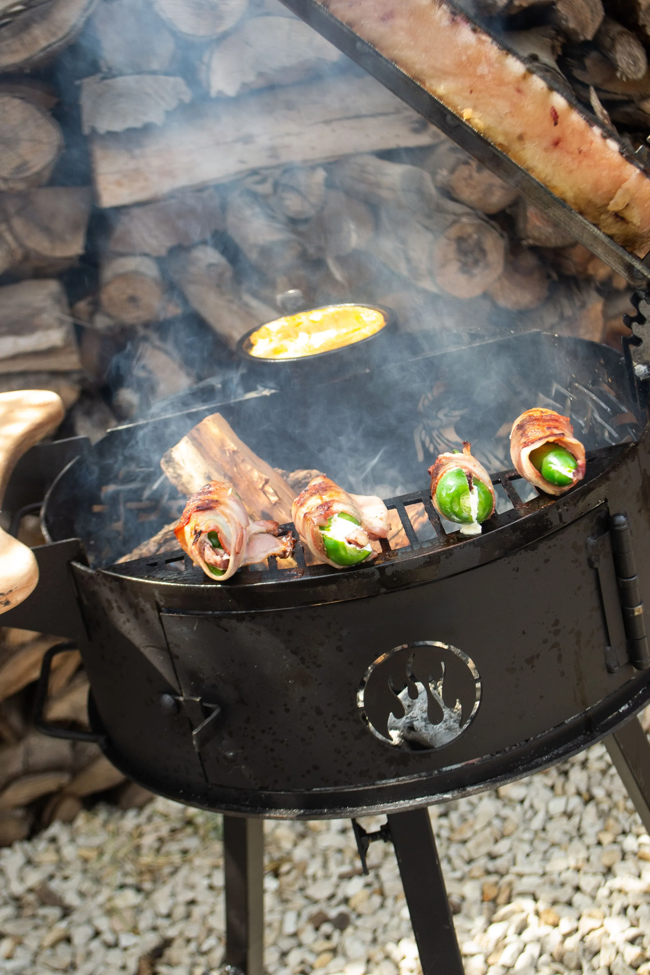 The firebox of an Alamo grill loaded with logs, beside the cast grate with the brand's flame cut out of it.