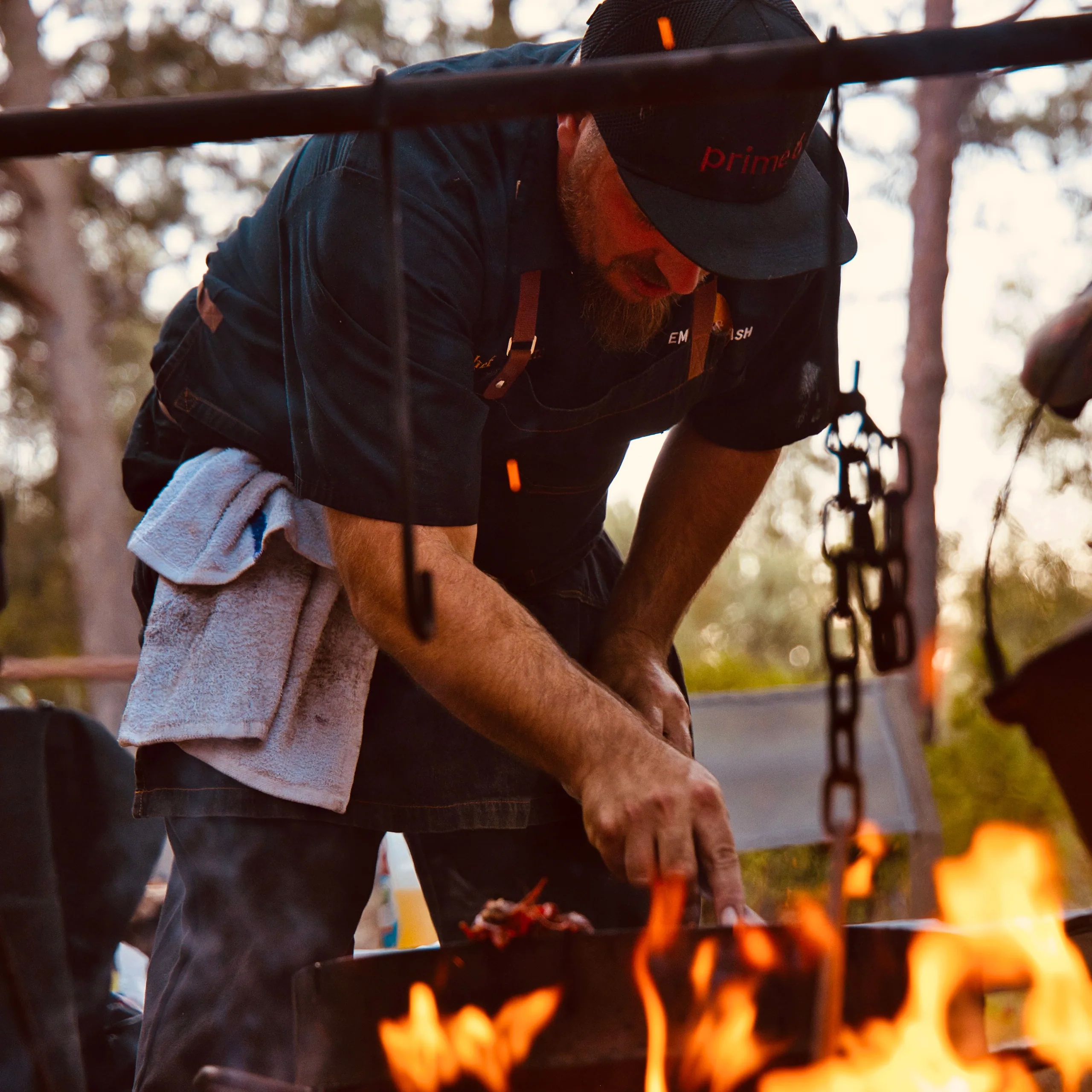 A chef leaning over a live fire at dusk