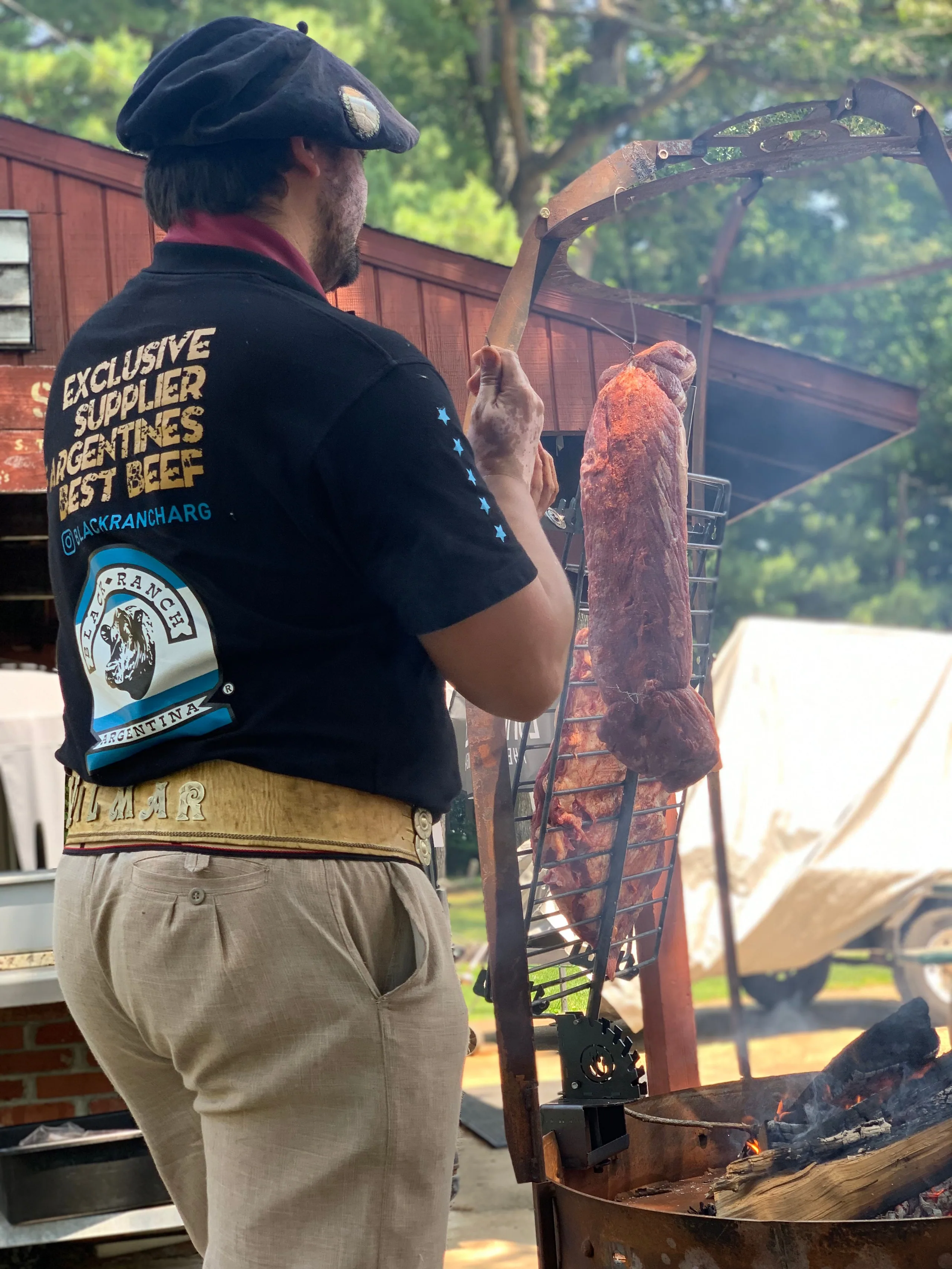 A chef in an Espíritu Parrillero shirt turning meat on the cross