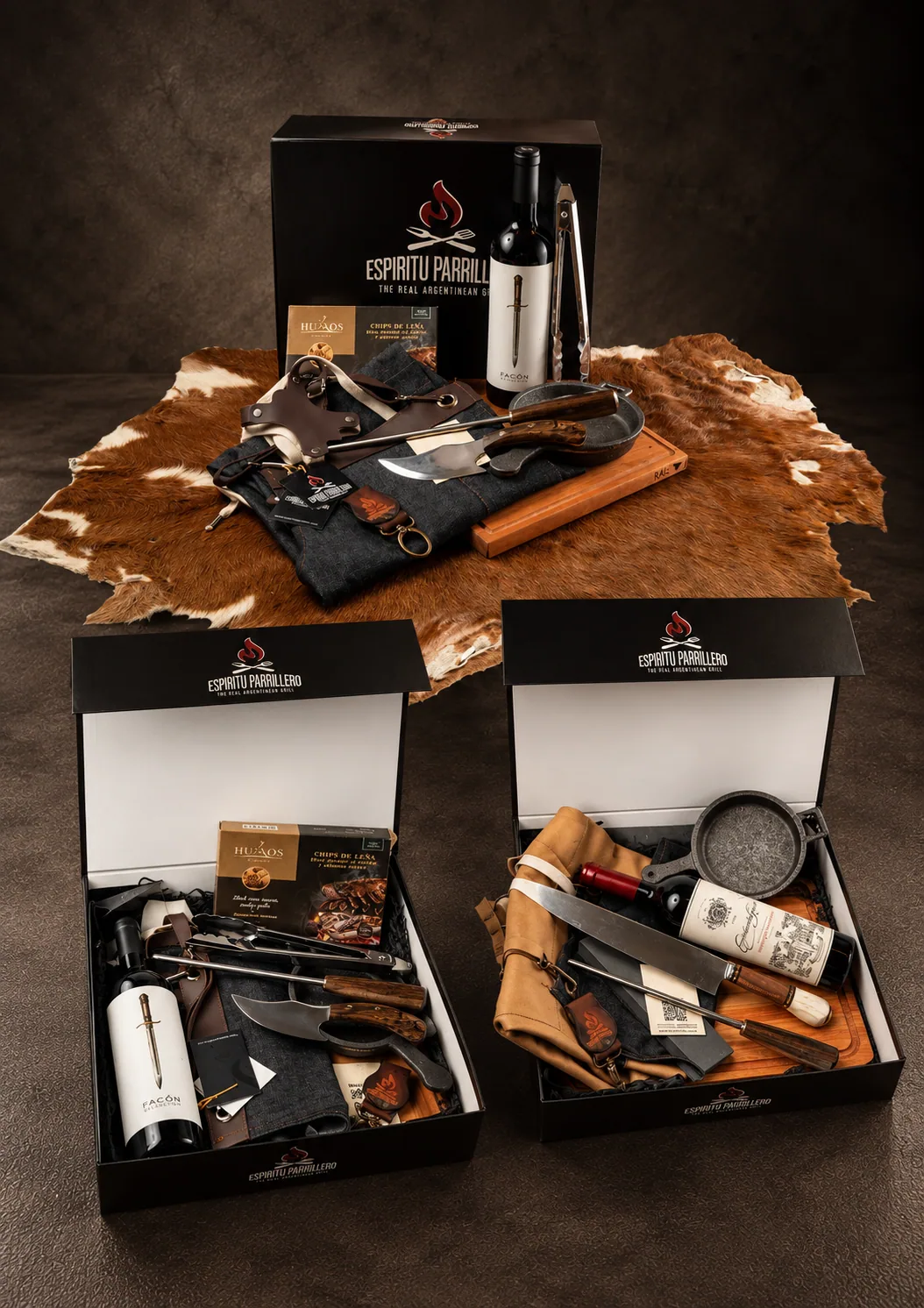 Three open Espíritu Parrillero gift boxes filled with knives, aprons, wine and grilling tools