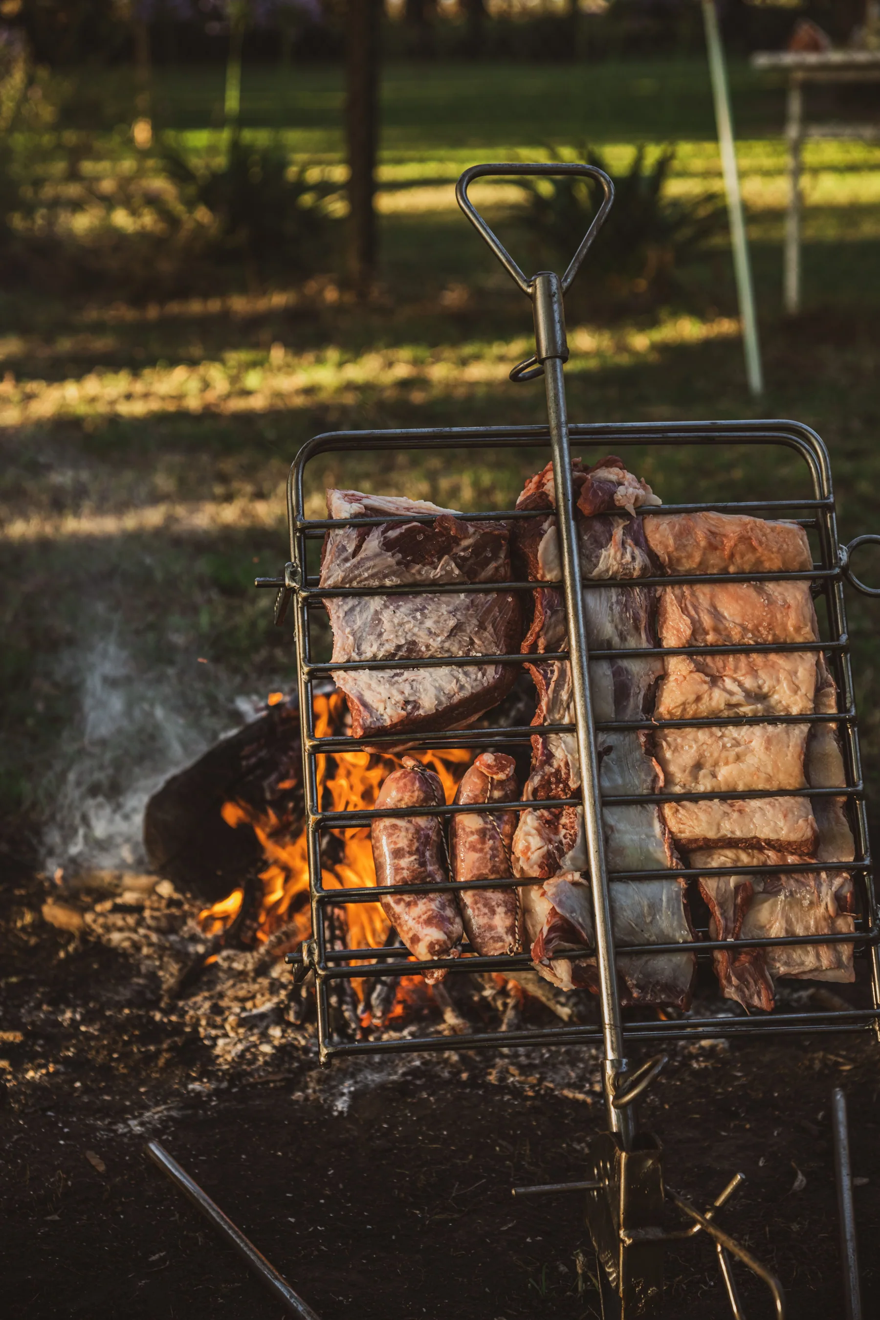 Asador Sostiene chico con costillar y chorizos sobre el fuego